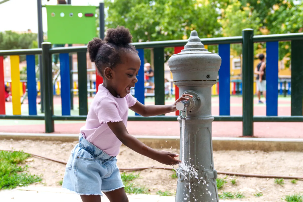 Radiant African girl happily splashing and playing with water in a city park fountain.